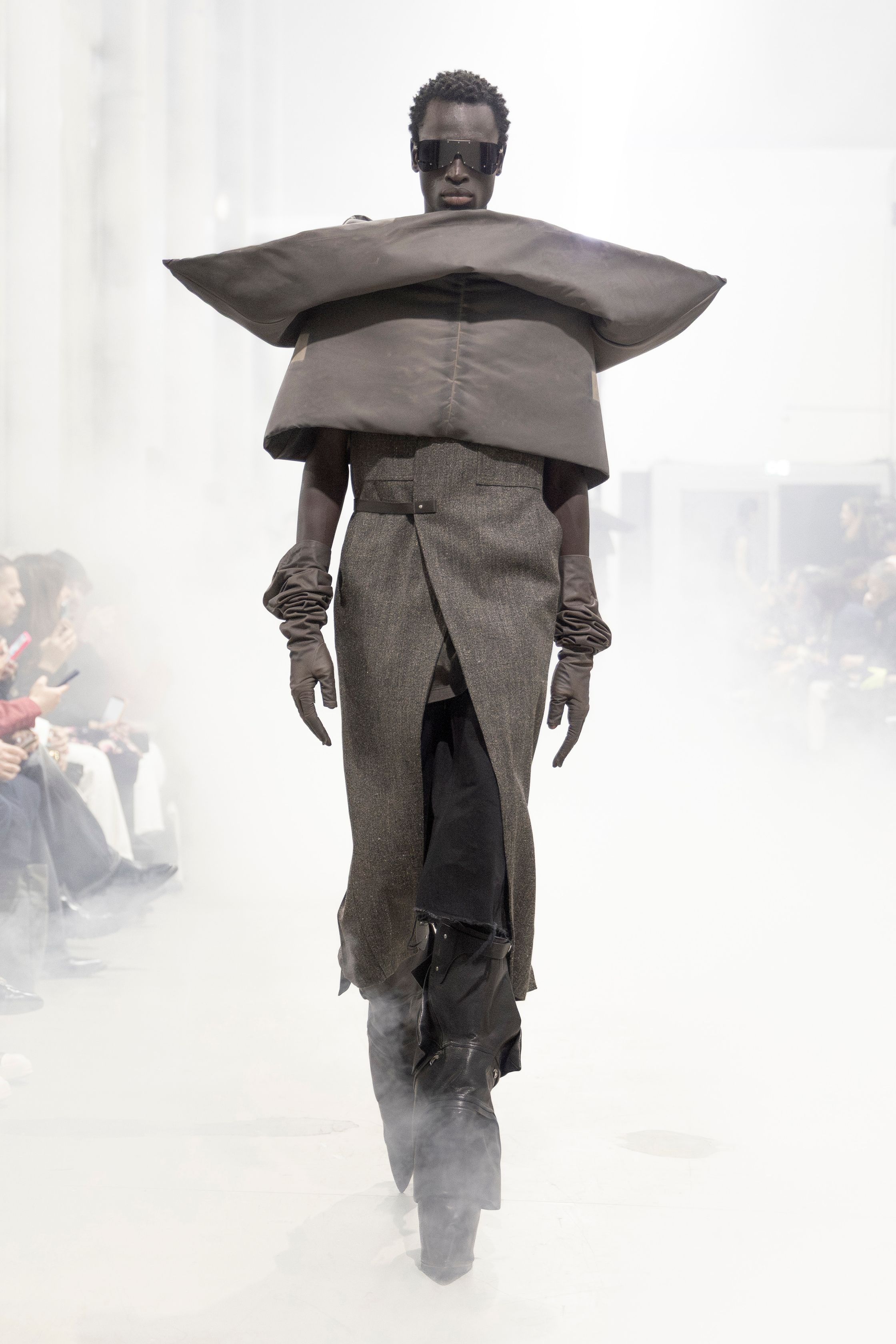 Rick Owens 2026秋冬延续其末世感与宗教式仪式美学。极端肩部结构、皮革与毛感材质在烟雾弥漫的空间中塑造出超越性别的强势身体。系列不再讨论日常，而是关于存在、力量与脆弱的对立统一。行走仿佛一种宣誓，服装成为精神铠甲，彰显Rick Owens一贯的黑暗崇高感-顽石频道趋势研究